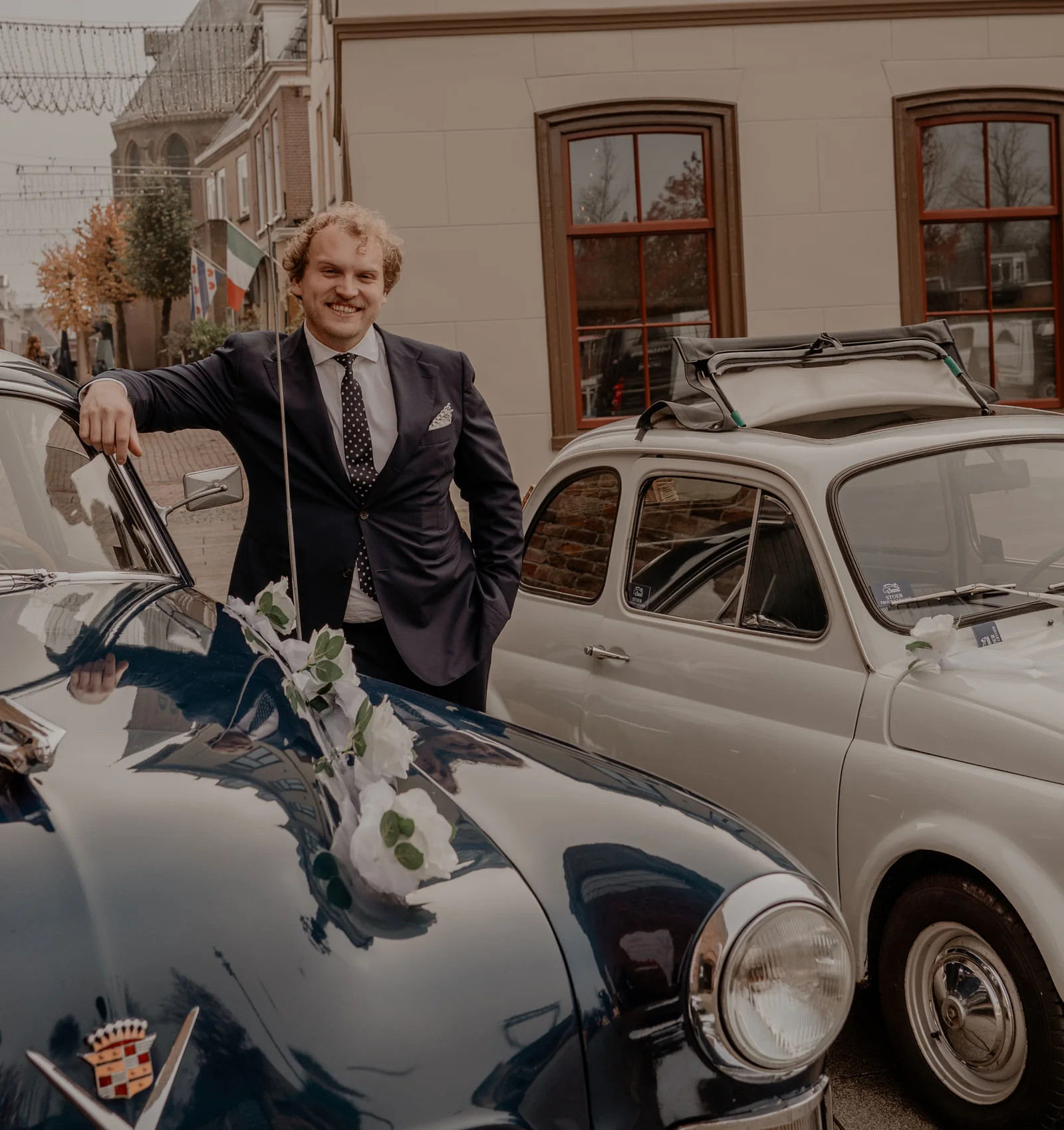 Jochem Stoer leunt lachend op de Cadillac, met de Fiat 500L naast hem